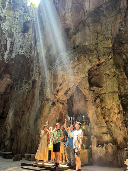A group of people standing on a stage in front of a cave with a waterfall. 5