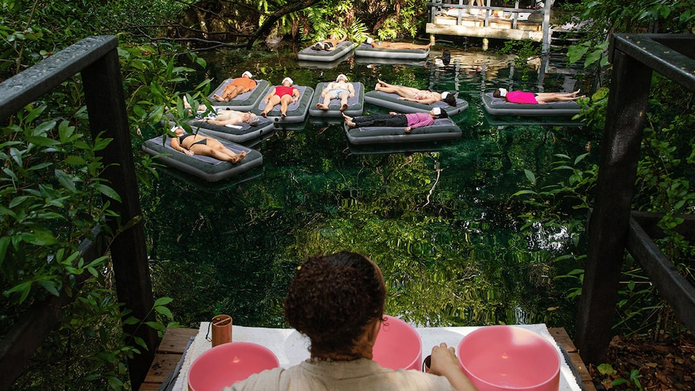 People relaxing on floating platforms in a lush, green outdoor setting. 3