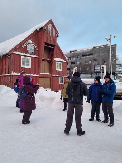 A group of people in winter clothing standing in front of a red building with a sign that reads 'Polarmuseet.' 4