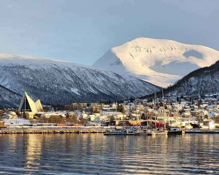 A snow-covered mountain, a town with buildings, and a body of water reflecting the scene. 2