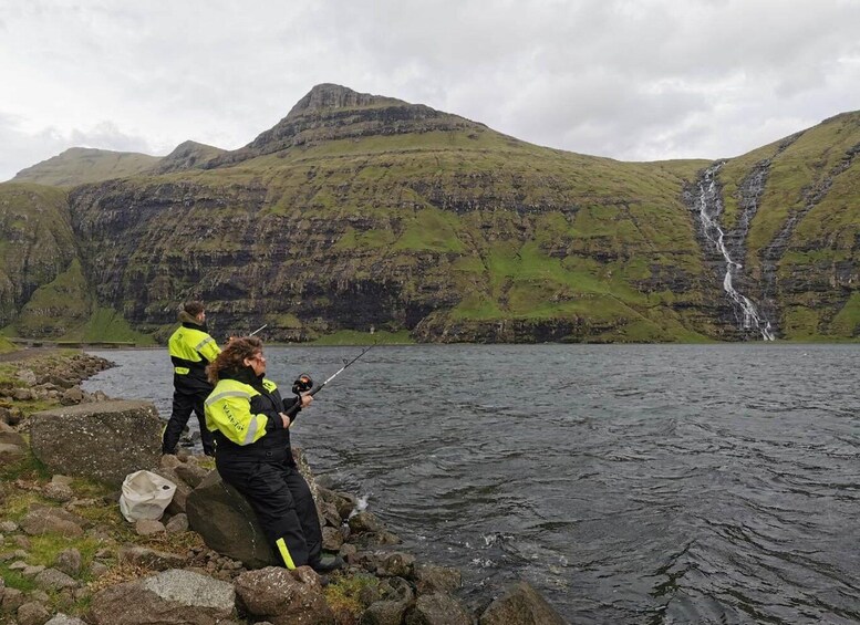 Three people fishing by a lake with a waterfall in the background. 5