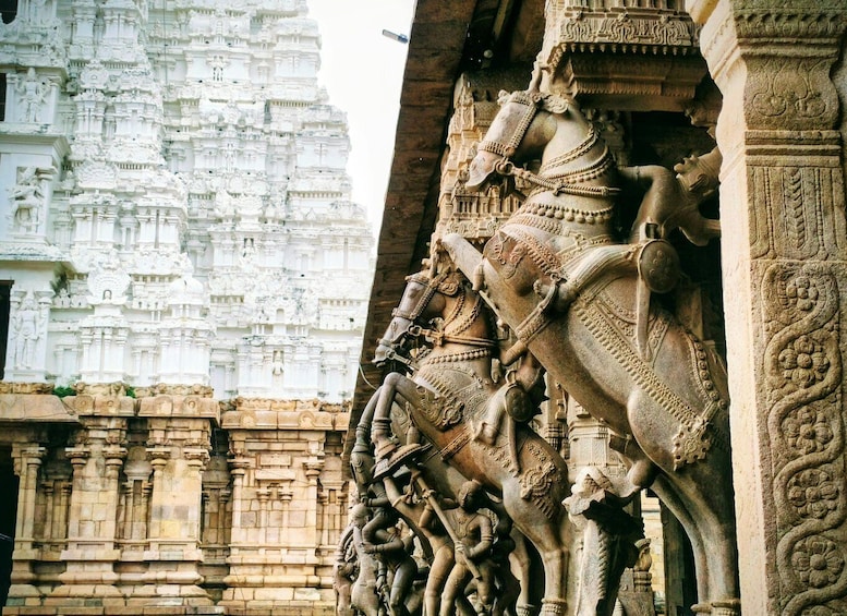 A detailed stone carving of a chariot with figures, set against a backdrop of a white temple structure. 1