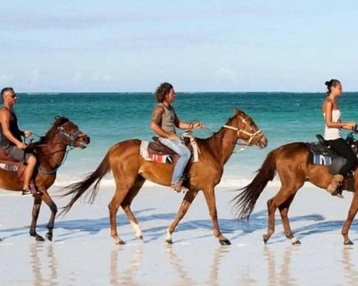 Three people riding horses on a beach. 5