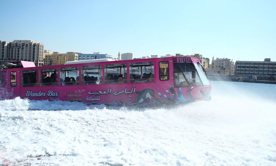 A pink bus labeled 'Wonder Bus Tours' driving through a snowy landscape with buildings in the background. 2