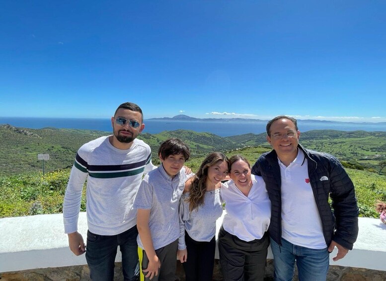 A group of people standing on a stone wall overlooking a coastal landscape with hills and the sea in the background. 5