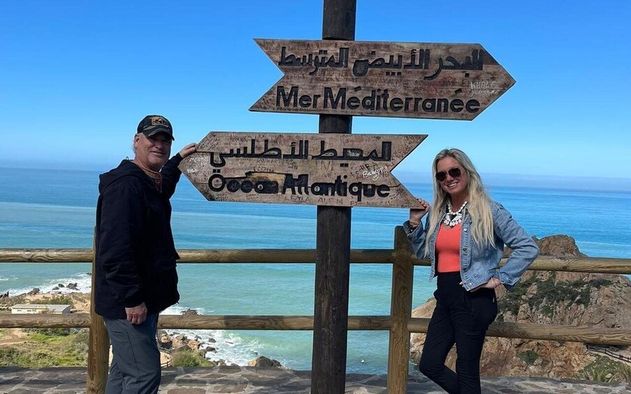 Two people standing by a wooden signpost with directions to Mer Mediterranee and Ocea Atlantique. 4