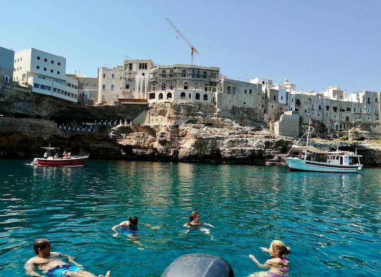 A coastal town with people swimming in the water, boats, and a construction crane in the background. 1