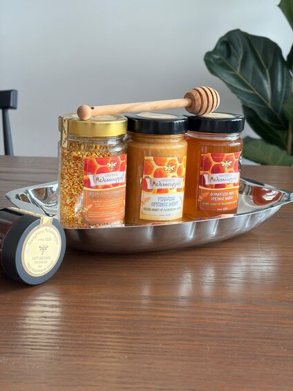 Three honey jars on a tray with a honey dipper and a beeswax container. 3
