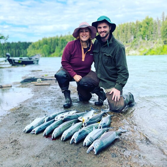 Two people standing by a river with several fish laid out on the ground. 4