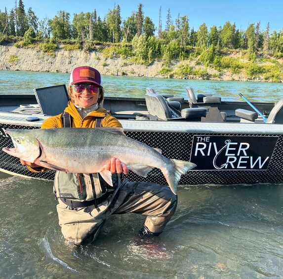A person holding a large fish on a boat named "The River Crew". 1