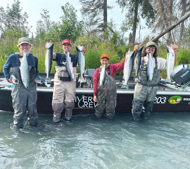 Four people holding fish on a boat with 'River Crew' written on the side. 2