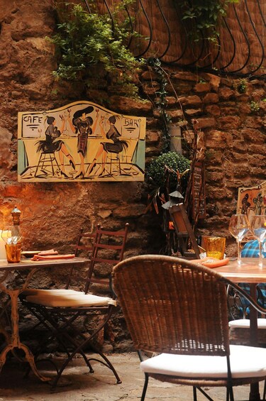 A rustic outdoor cafe with stone walls, wooden chairs, and a mural depicting a cafe scene. 4