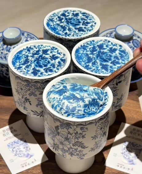 A set of four ceramic cups with blue floral patterns, one of which is being held by a wooden spoon. 1
