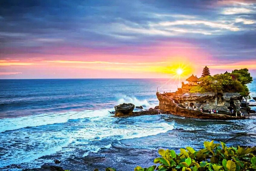 A sunset over the ocean with a traditional pagoda on a rocky outcrop. 1