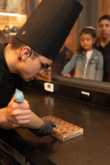 A person wearing a black hat and gloves, working with a waffle maker on a counter. 4