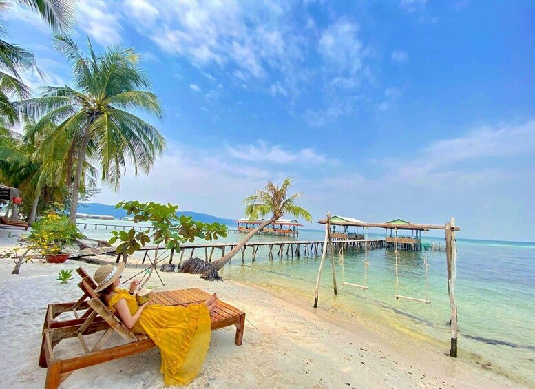 A beach with wooden lounge chairs, palm trees, and a wooden pier extending into the ocean. 1