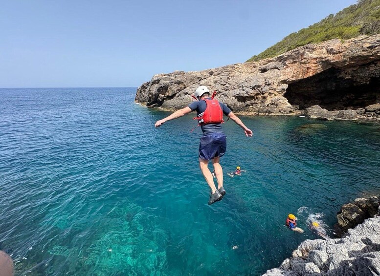 A person jumping into clear blue water near rocky cliffs. 1