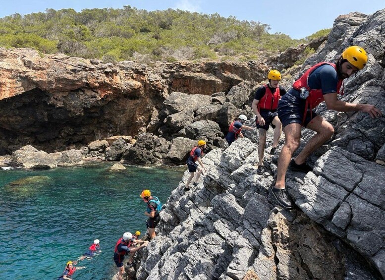 A group of people climbing a rocky cliff by a body of water. 5