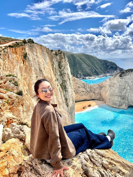 A person sitting on a rocky cliff overlooking a coastal landscape with cliffs and a beach. 4