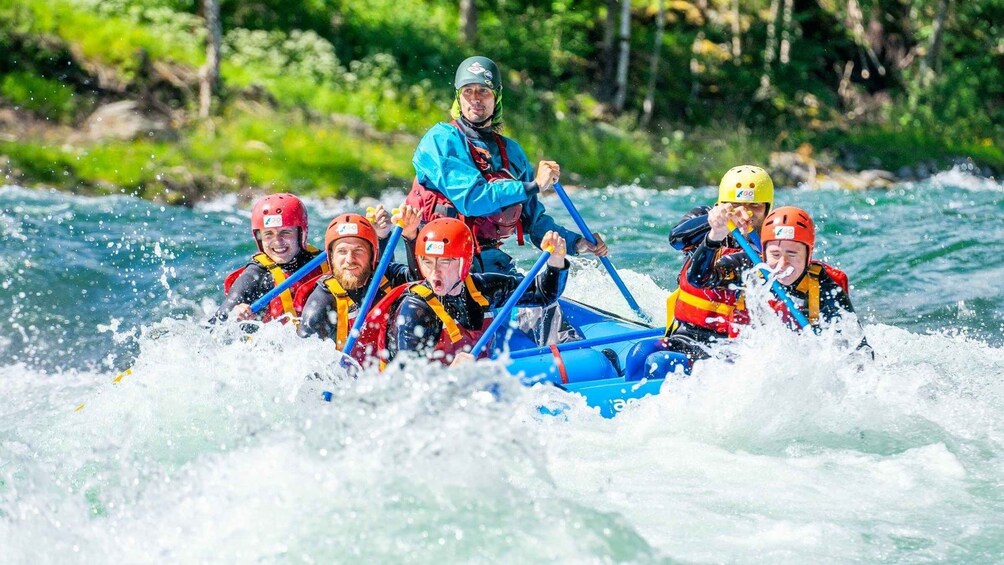A group of people in a blue raft navigating through white water rapids. 1