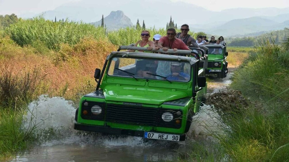 A green Land Rover driving through a shallow water crossing surrounded by tall grass and hills. 4