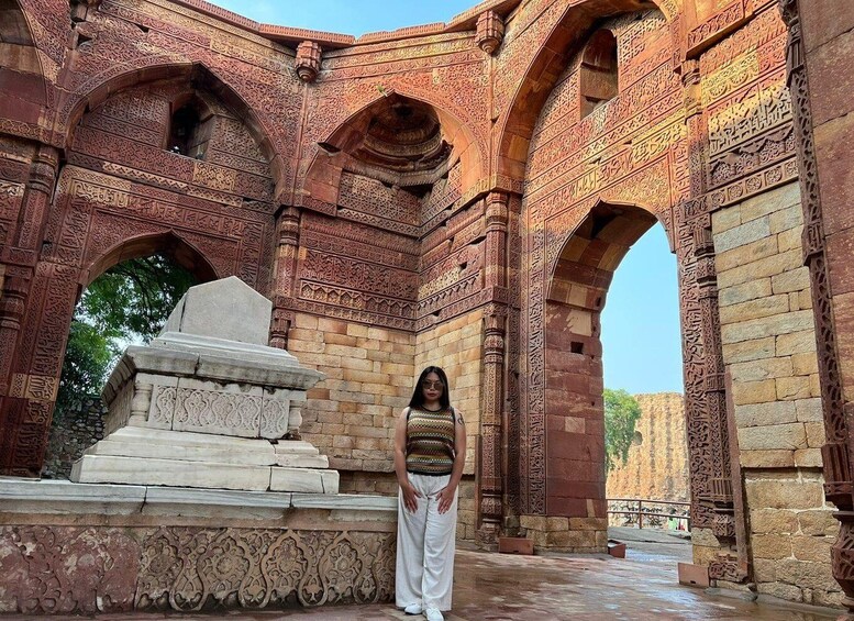 A person standing in front of a large, intricately carved stone structure with arches and detailed patterns. 4