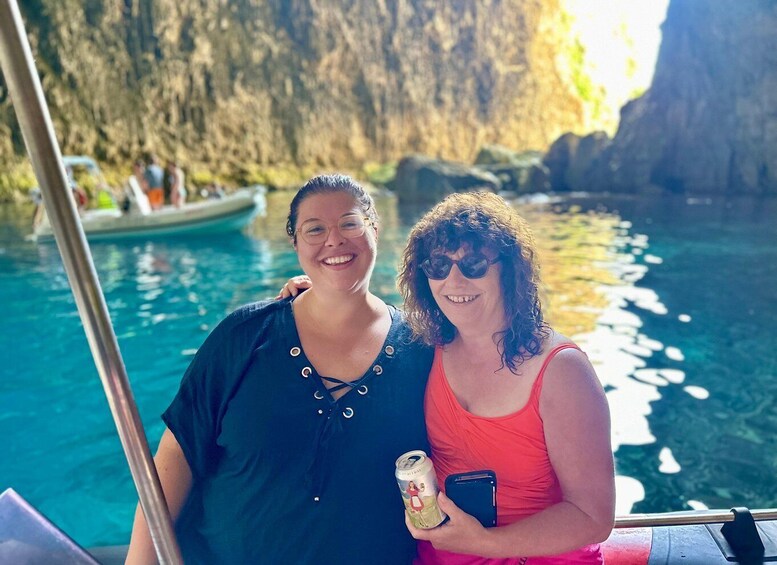 Two people on a boat near a clear blue water body with rocky cliffs in the background. 4