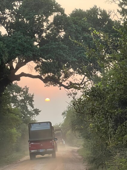A red vehicle driving on a dusty road with a sunset in the background. 3