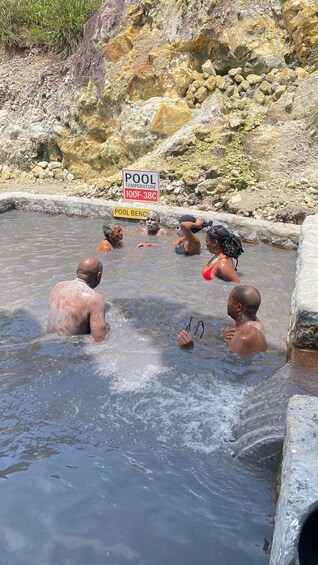 A group of people in a natural hot spring with signs indicating the temperature range. 5