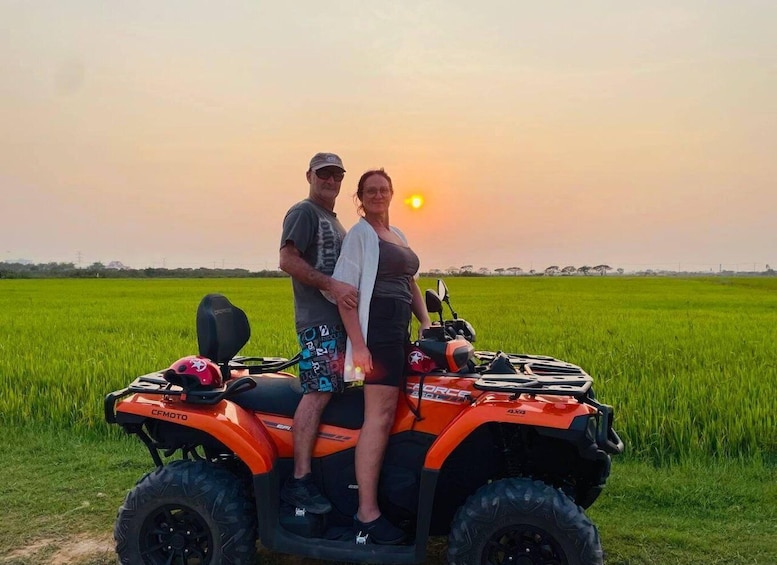 A man and a woman on an orange ATV in a green field with a sunset in the background. 2