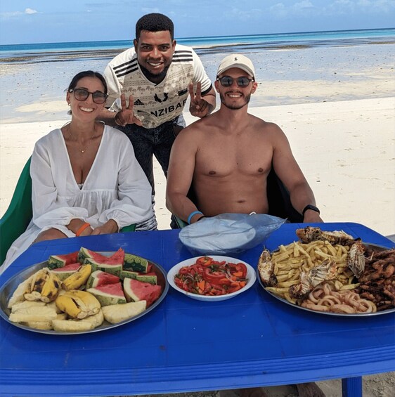 Escena de playa con una mesa llena de comida, incluyendo frutas, verduras y mariscos. 4