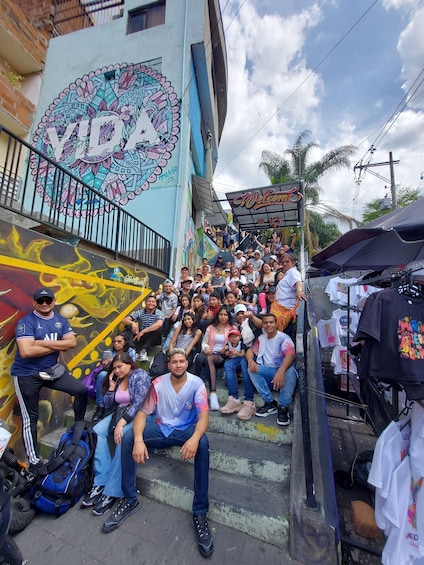 A group of people sitting on steps in an urban area with colorful graffiti and a sign that reads "Welcome". 5