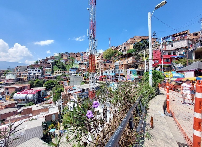 A densely packed hillside settlement with colorful buildings, a prominent red telecommunications tower, and a street with orange safety barriers. 5