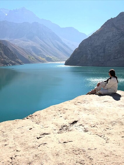 A person sitting on a rocky outcrop overlooking a turquoise lake with mountains in the background. 2