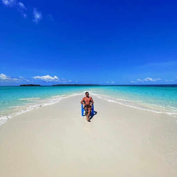 A man walking on a beach with clear turquoise water and a clear blue sky. 1