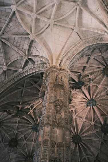 A Gothic-style cathedral ceiling with ribbed vaults and a central column featuring intricate carvings. 3