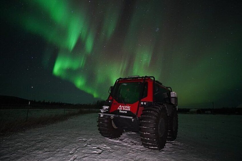 A red vehicle on a snowy surface with the Northern Lights in the background. 2