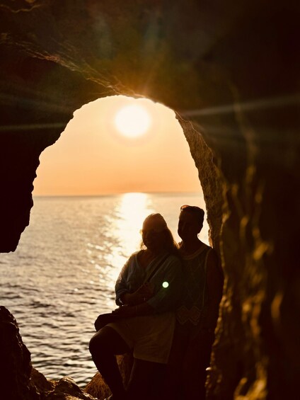 Deux personnes sont assises dans une grotte, avec un coucher de soleil en arrière-plan. 3