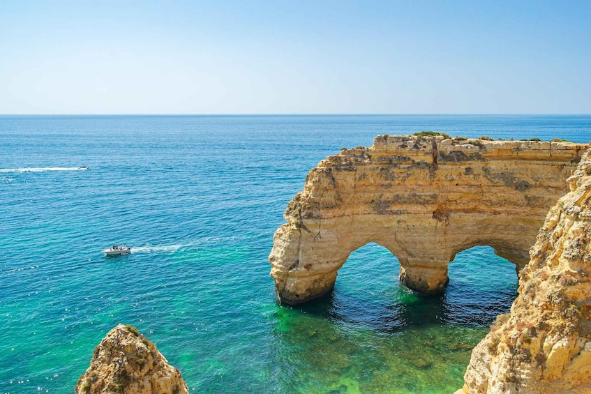 Un paysage côtier caractérisé par une formation rocheuse imposante, sur laquelle se trouve une arche naturelle surplombant des eaux d’un bleu cristallin. 4