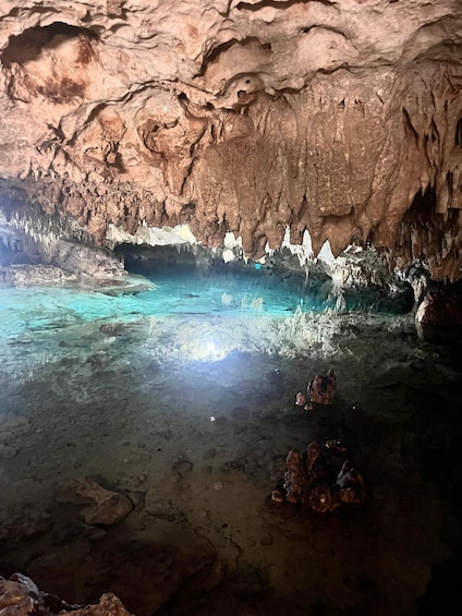 A cave with stalactites and stalagmites, clear water, and rocks on the floor. 4