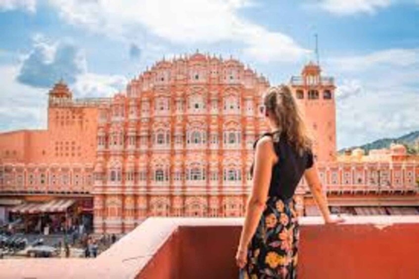 A woman standing on a balcony overlooking a large, ornate building with multiple towers and intricate architectural details. 3