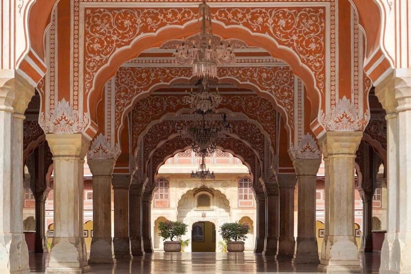 An ornate architectural corridor with arches and columns, a chandelier, and potted plants. 5
