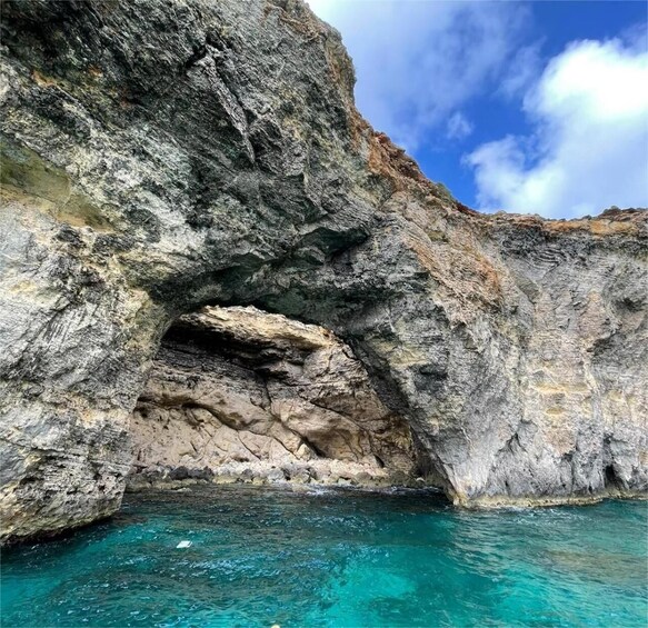 A rocky cliff with a cave opening into turquoise water. 1