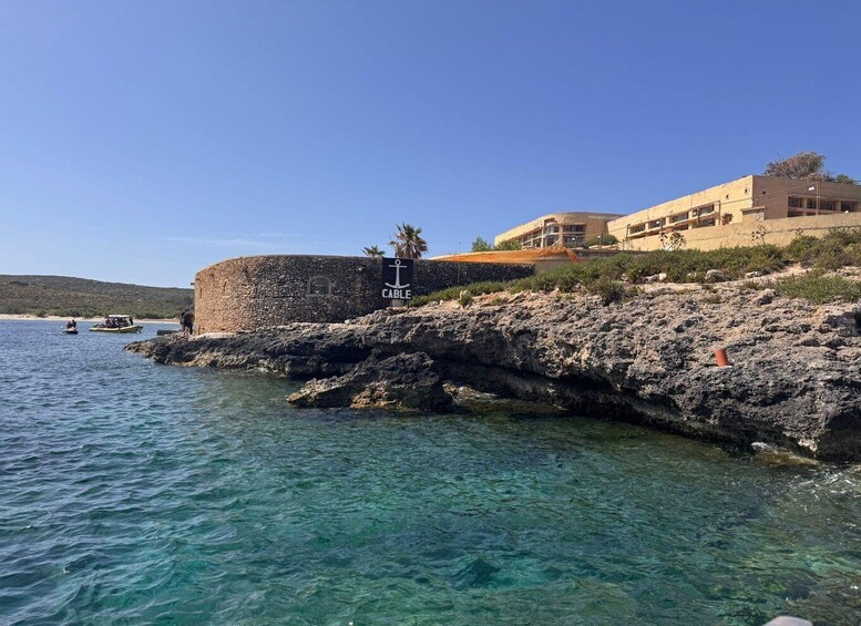 A coastal scene with clear water, a stone wall, and a building with a sign reading 'Cable'. 3