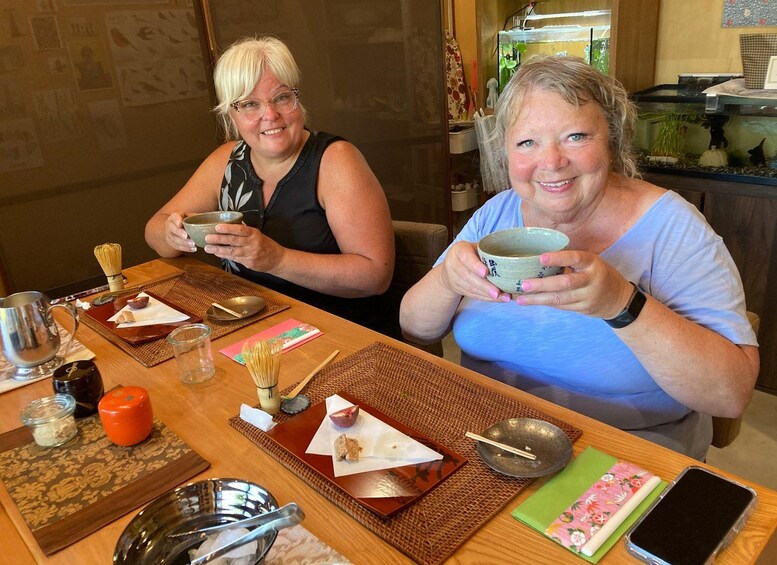 Two people sitting at a table with traditional Japanese tea ceremony utensils. 2