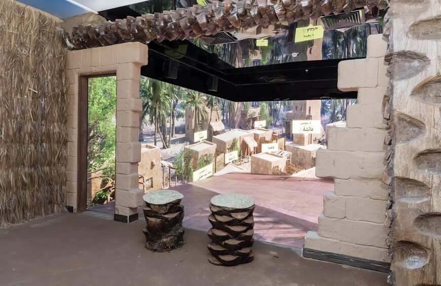 An indoor exhibit with a tropical theme, featuring a model village, stone stools, and a thatched wall. 5