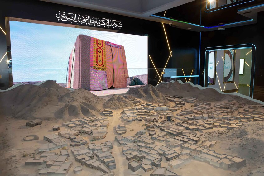 A model of a desert settlement with a large screen displaying a traditional fabric. 2