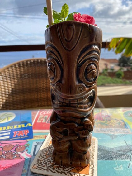 A tiki mug with a straw and a flower on top, placed on a coaster with a map and a book. 3