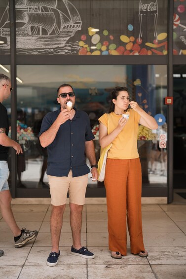 Due persone mangiano coni gelato davanti a un negozio con decorazioni colorate e un'insegna Coca-Cola. 1