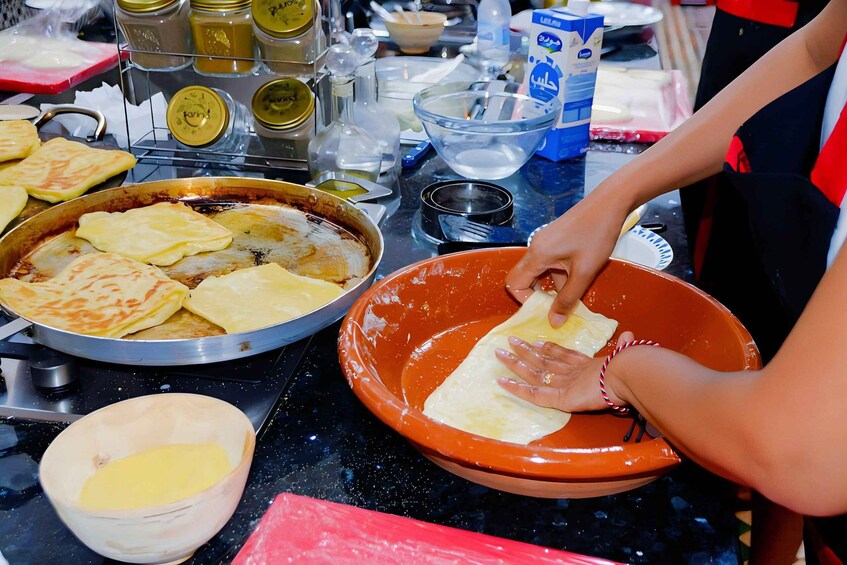 A person preparing food, specifically rolling dough into flatbreads, with various kitchen items and ingredients visible. 1